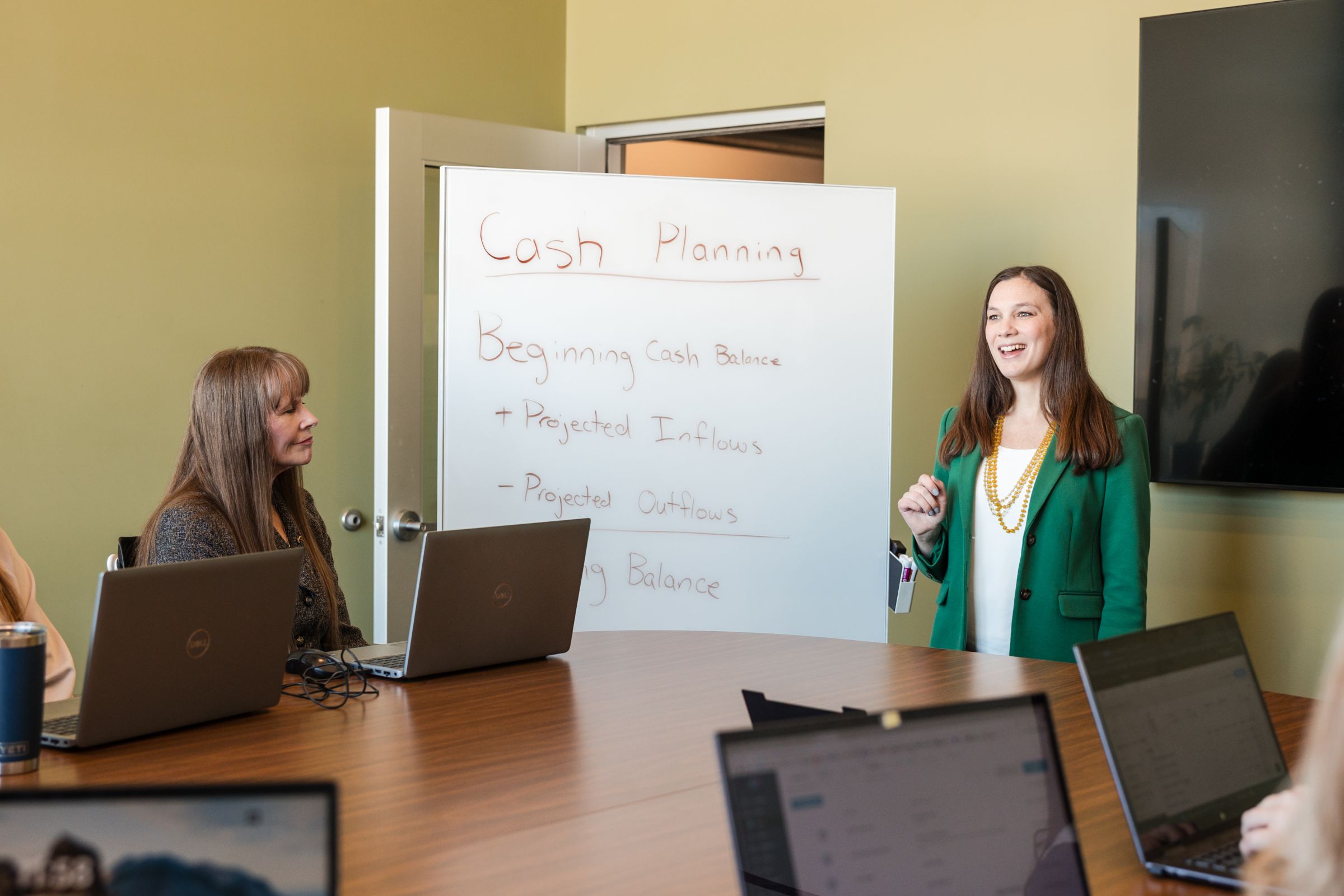 Cash planning meeting: Woman presenting financial services strategy to team with laptops in conference room. Step-by-step guide.