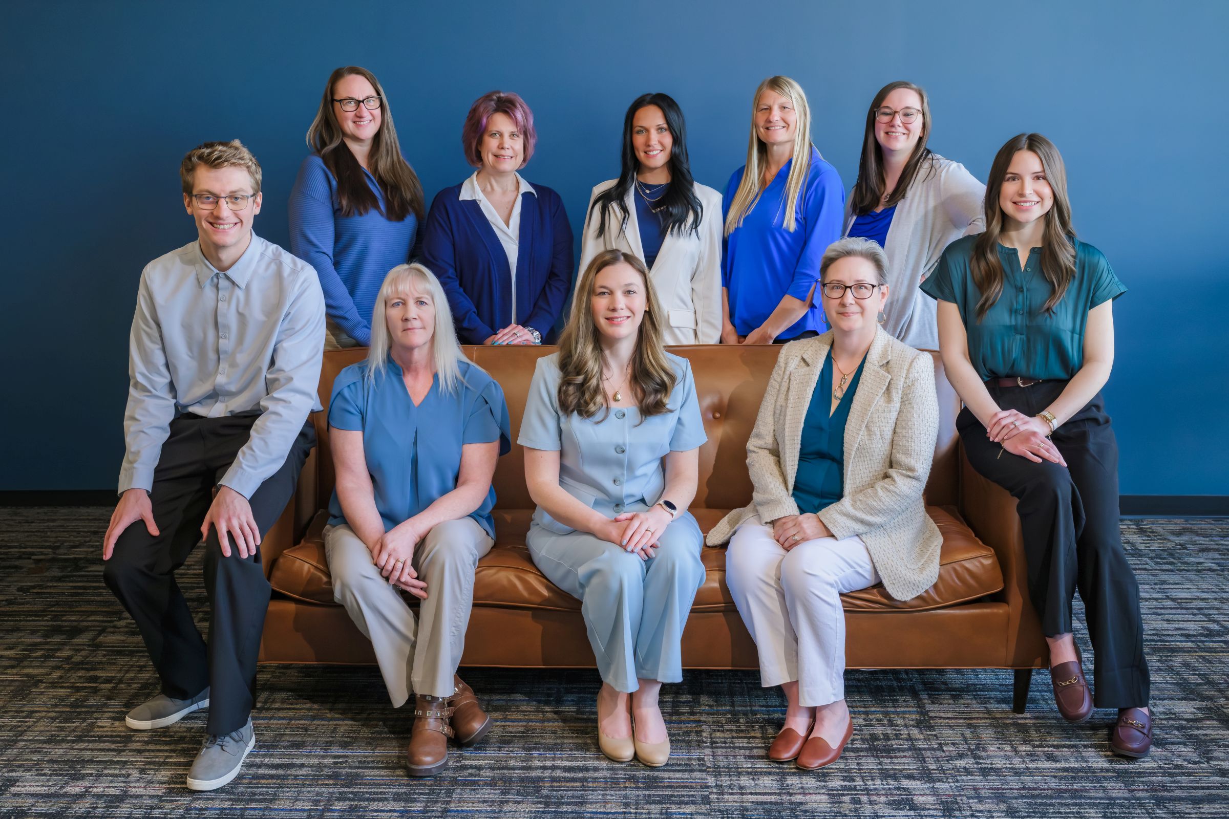The Step By Step Accounting team, seated on or standing behind a brown leather couch against a blue wall.