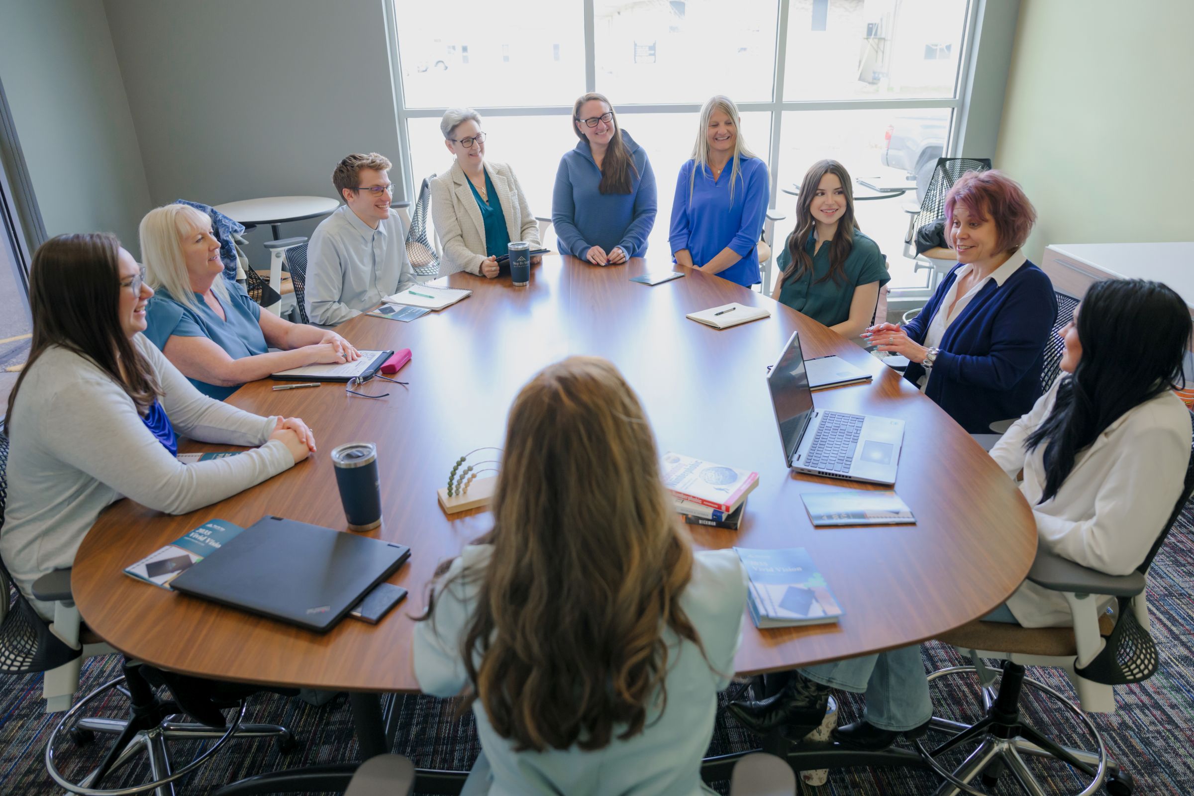 A happy group of businesspeople sit around a conference room table and talk.