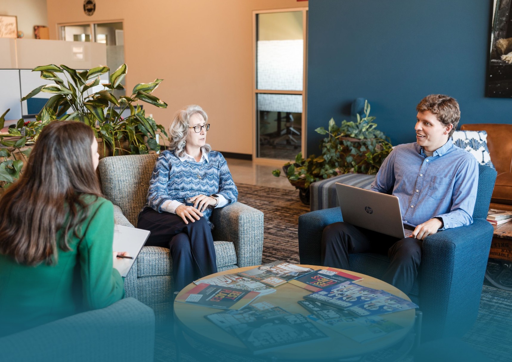 Three professionals in office lounge in a discussion, with laptop and brochures. Teamwork and collaboration.