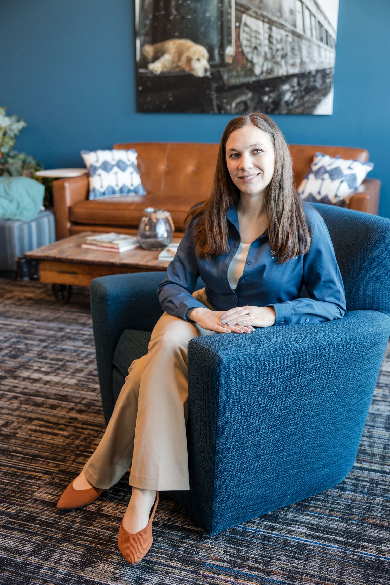 Woman in a blue shirt and tan pants sits on a blue chair in an office waiting area.